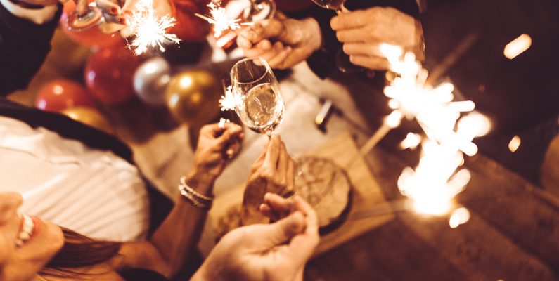 photo of people holding sparklers and wine glasses at a dinner party